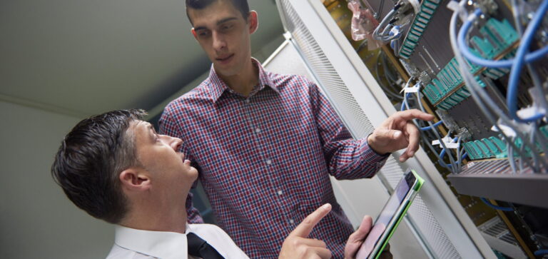 Two male IT workers discussing details of new technology, while installing equipment in a server room